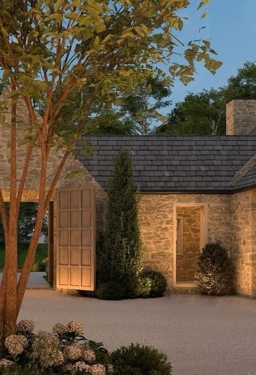 Stone wall, a timber door, and gravel under a tree at dusk.